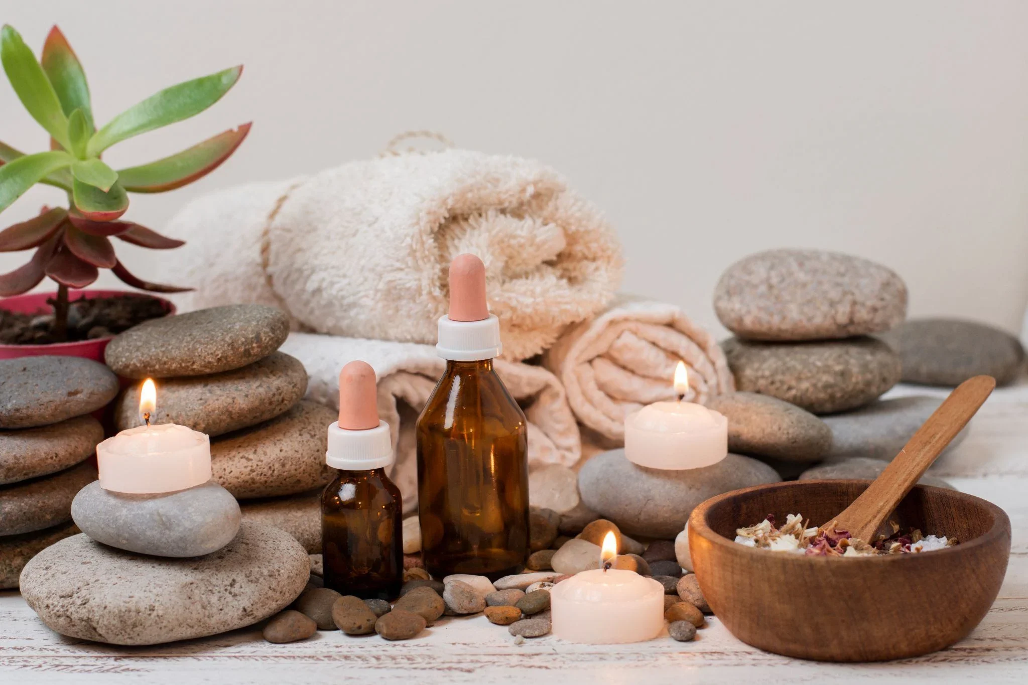Spa arrangement with stacked stones, essential oil bottles, lit candles, rolled towels, and a small wooden bowl.