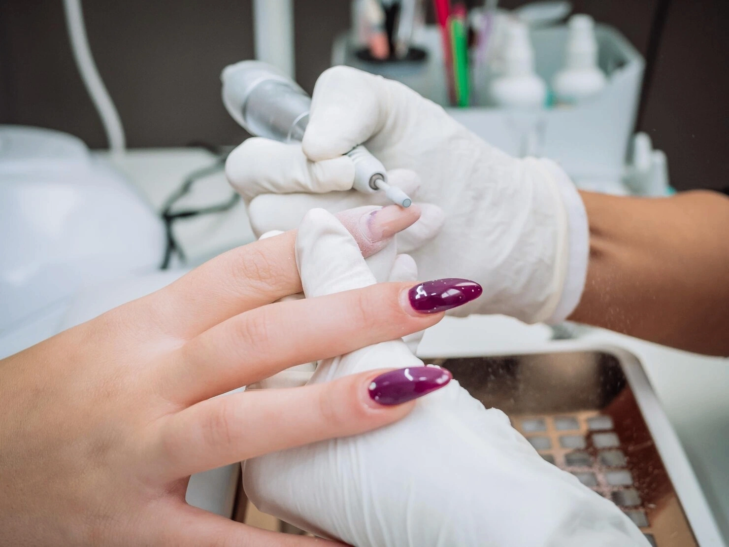 Nail technician filing and shaping a set of glossy purple nail enhancements during a professional nail appointment.